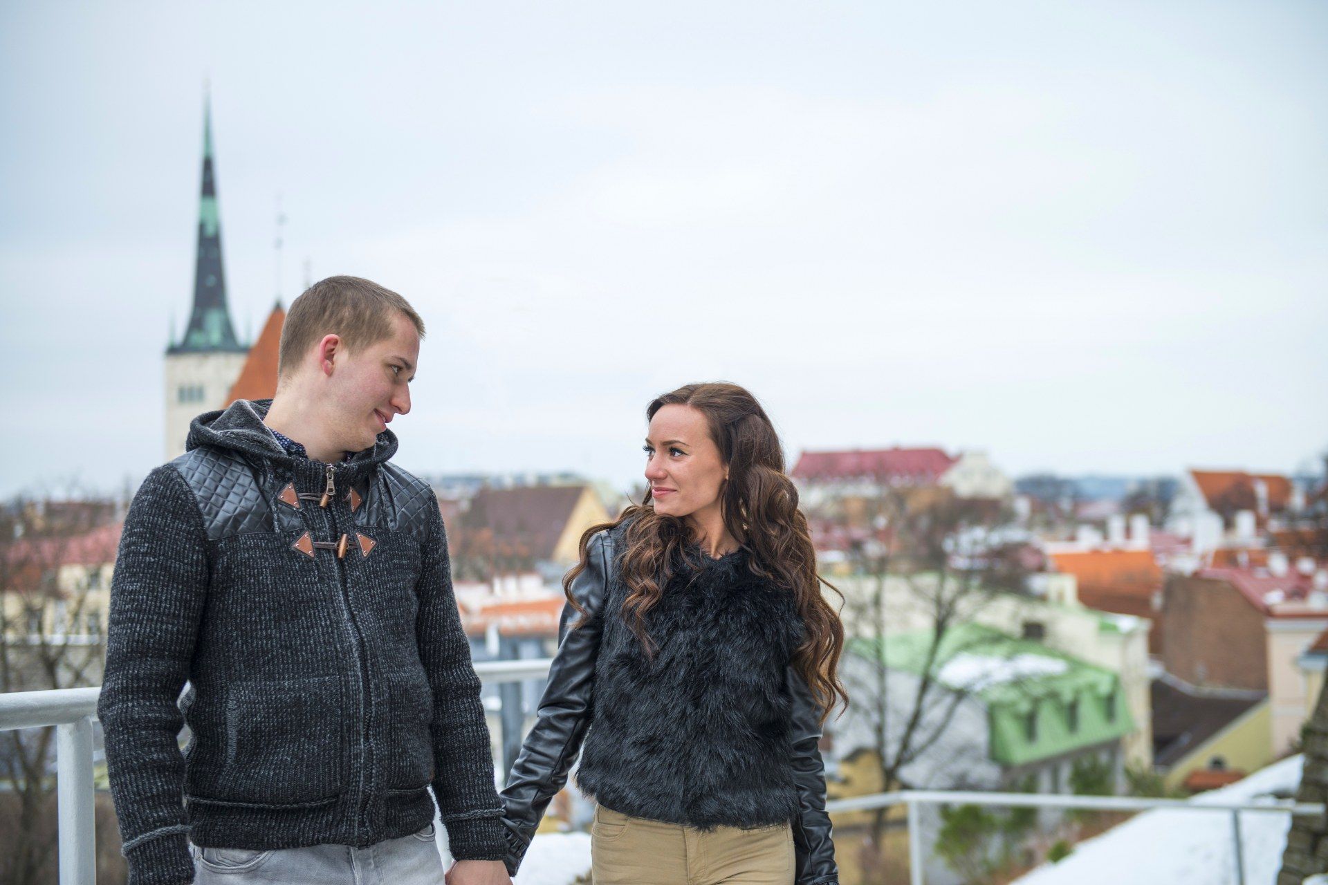 Pareja joven tomada de la mano con los tejados del casco antiguo de Tallin al fondo